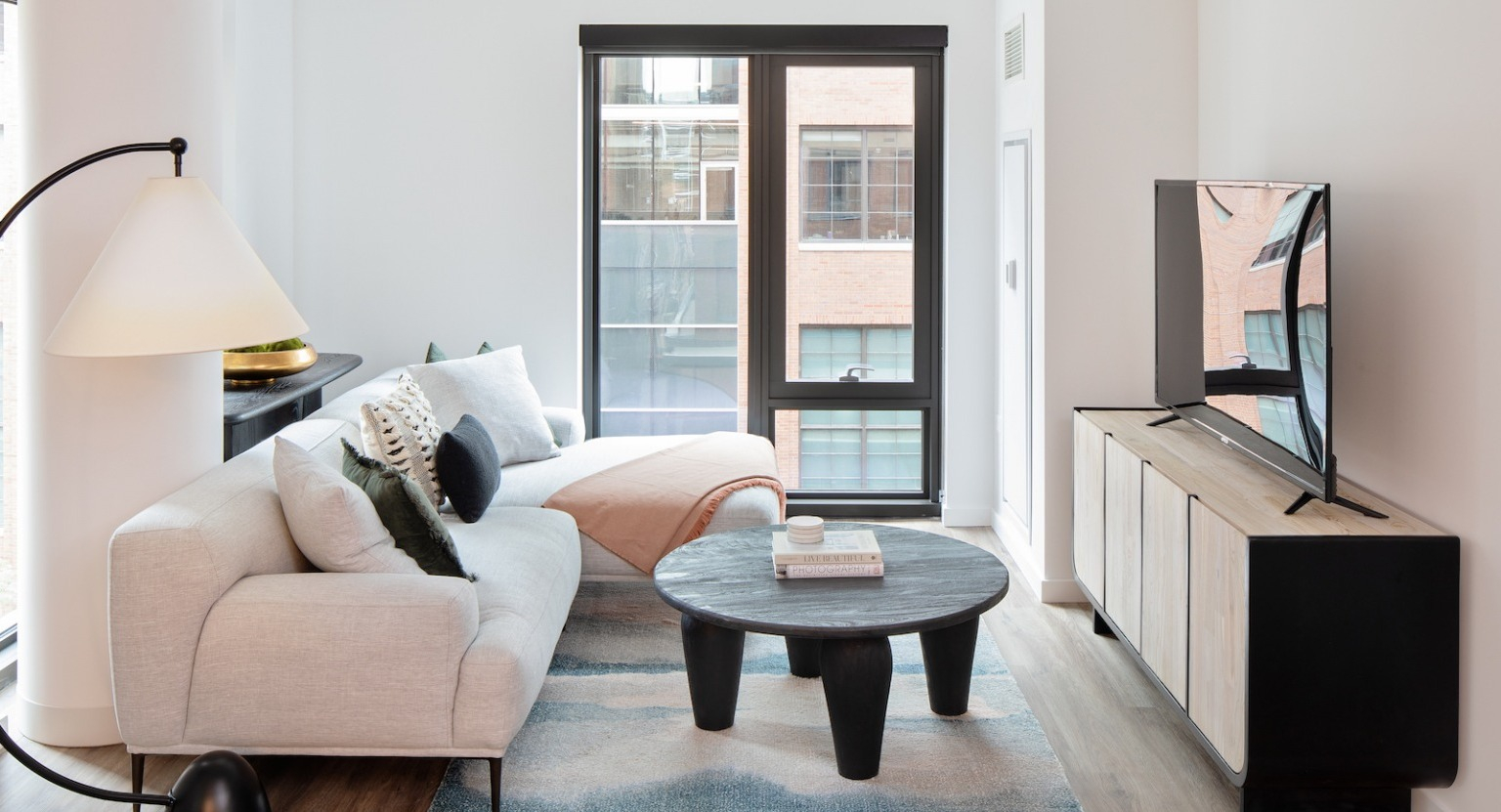 Modern and cozy living room with a large sofa, accent rug, stylish coffee table, and large window at One Six Six