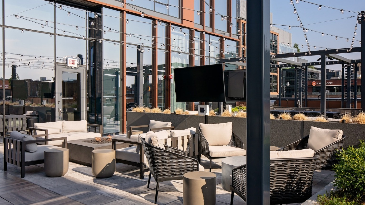 Inviting rooftop lounge with a fire pit, outdoor television, comfortable seating, and string lights at One Six Six