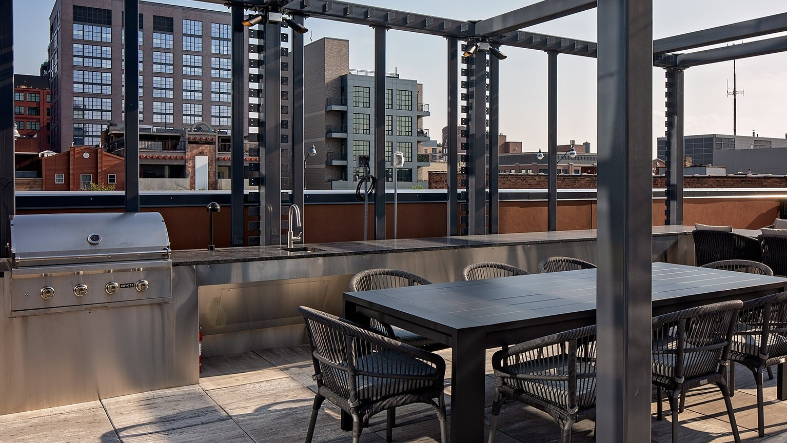 Outdoor rooftop dining and grilling area with a large table, chairs, and a built-in stainless steel grill at One Six Six