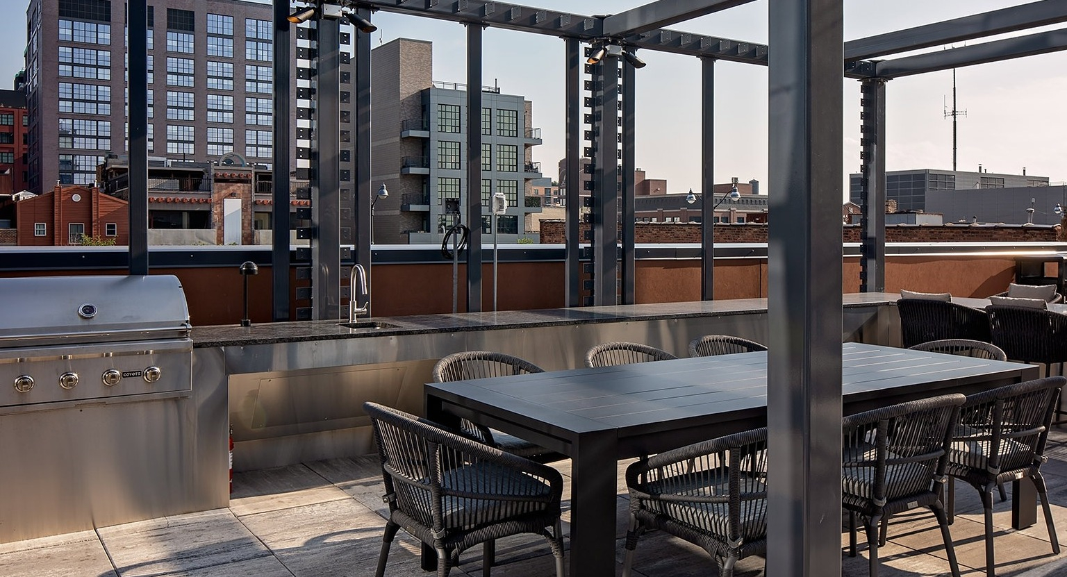 Outdoor rooftop dining and grilling area with a large table, chairs, and a built-in stainless steel grill at One Six Six