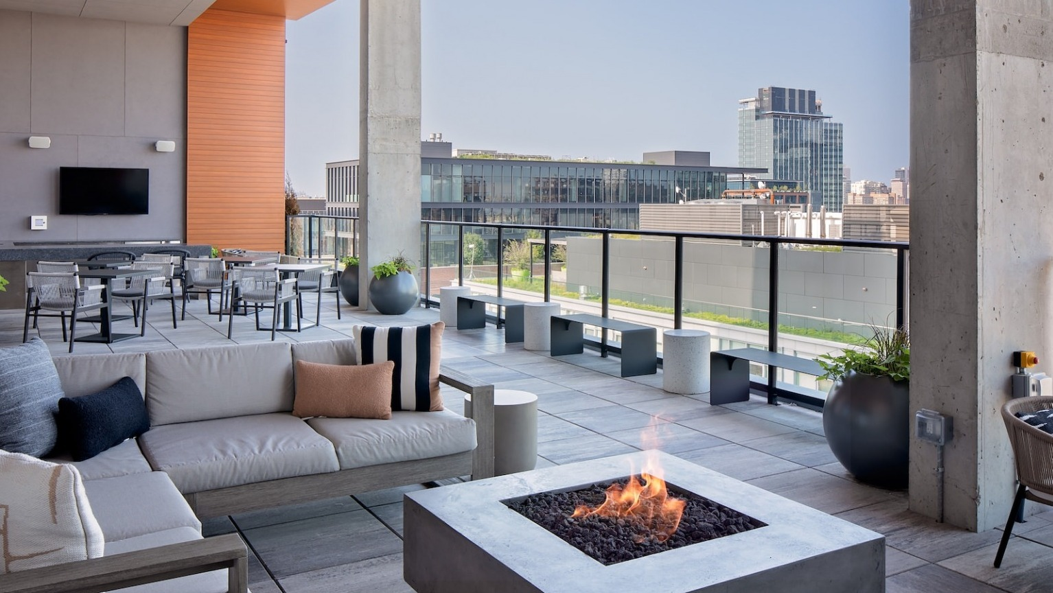 Expansive rooftop lounge with a modern fire pit, comfortable sofas, dining area, and city skyline views at One Six Six