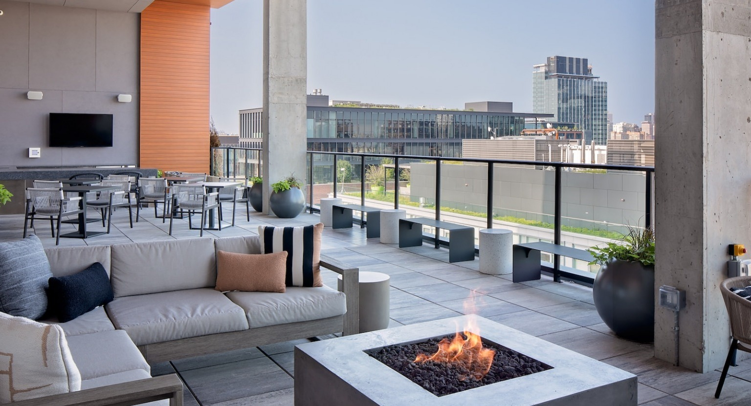 Expansive rooftop lounge with a modern fire pit, comfortable sofas, dining area, and city skyline views at One Six Six