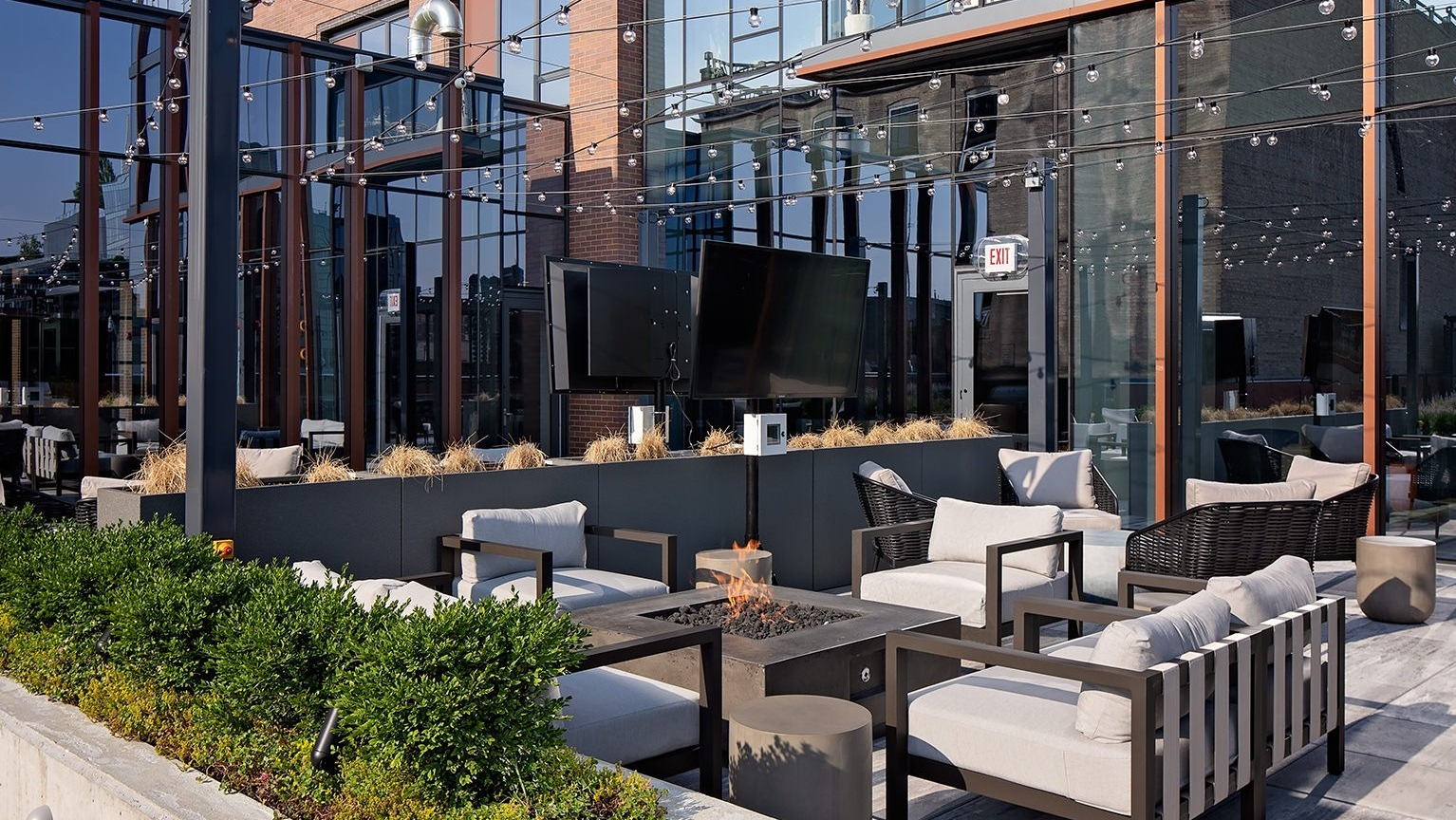 Stylish rooftop outdoor seating area with multiple fire pits, comfortable lounges, and lush greenery at One Six Six
