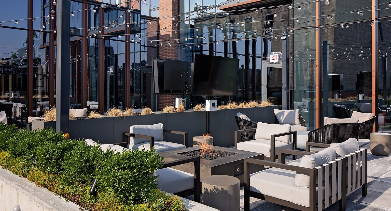 Stylish rooftop outdoor seating area with multiple fire pits, comfortable lounges, and lush greenery at One Six Six