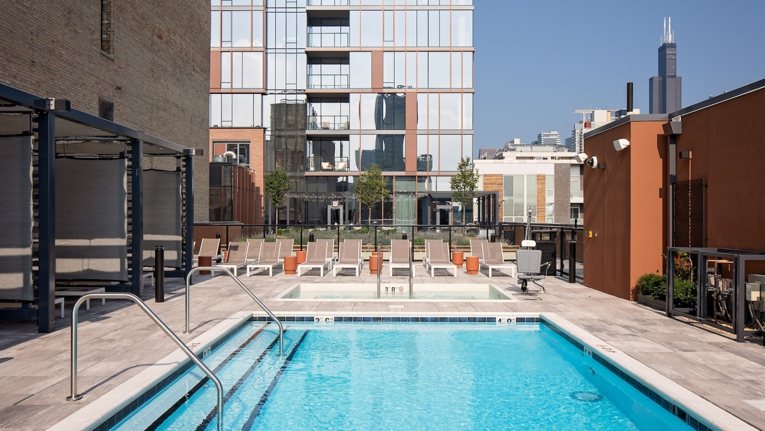 Sunny rooftop pool with lounge chairs, surrounded by modern buildings and a clear blue sky at One Six Six