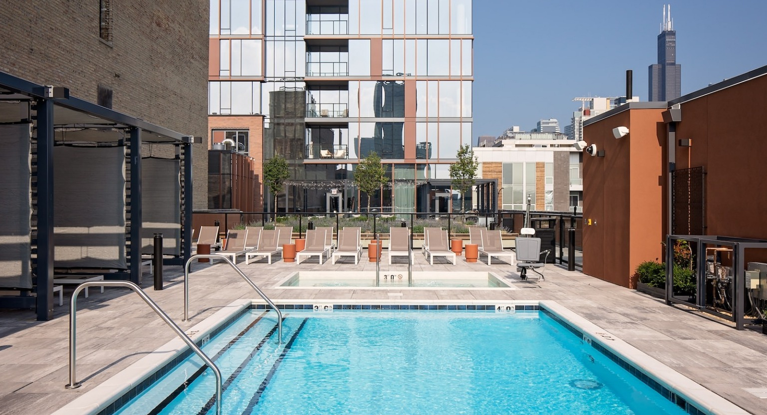 Sunny rooftop pool with lounge chairs, surrounded by modern buildings and a clear blue sky at One Six Six
