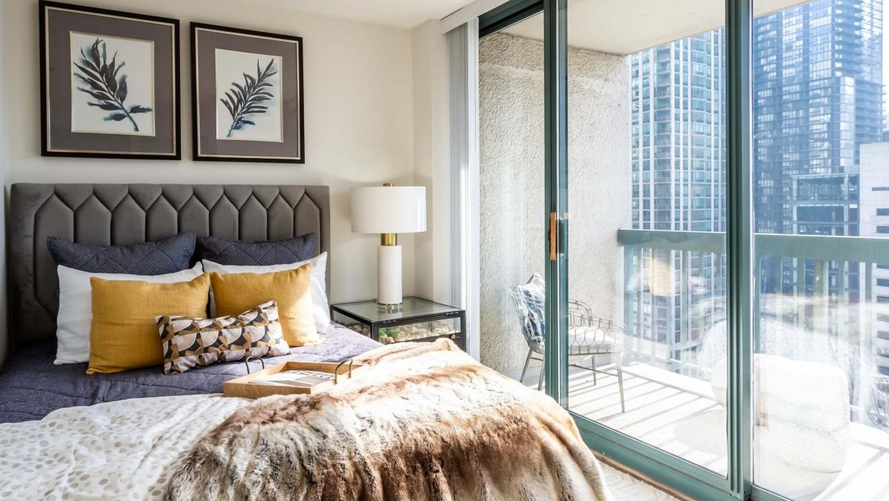Sunlit bedroom at One Superior Place Apartments featuring modern décor, warm bedding, and balcony access with high-rise city views