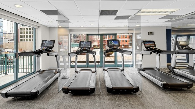 Cardio gym at One Superior Place Apartments featuring treadmills lined up by floor-to-ceiling windows with Chicago skyline views