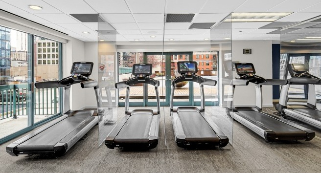 Cardio gym at One Superior Place Apartments featuring treadmills lined up by floor-to-ceiling windows with Chicago skyline views