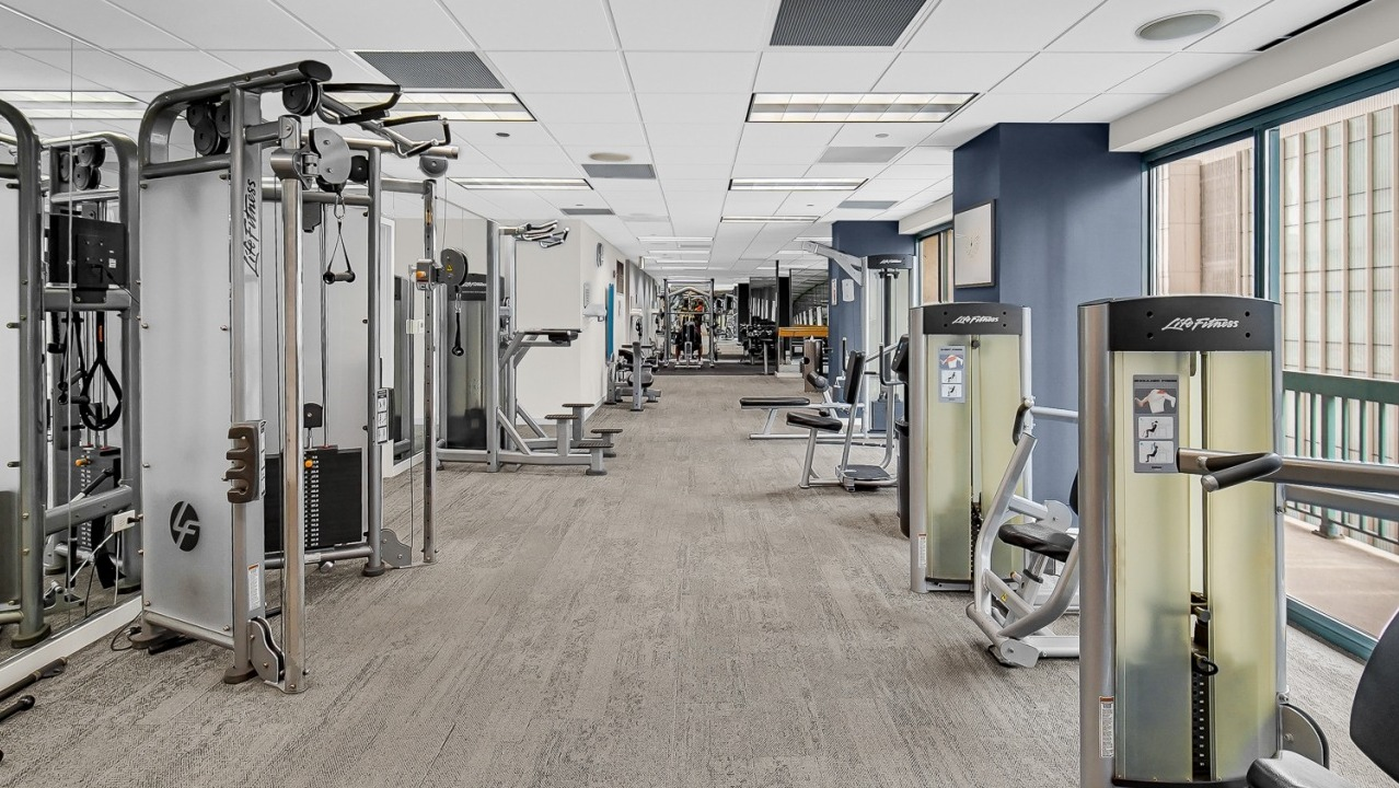 Fitness center at One Superior Place Apartments with Life Fitness machines, free weights, and large windows with city views