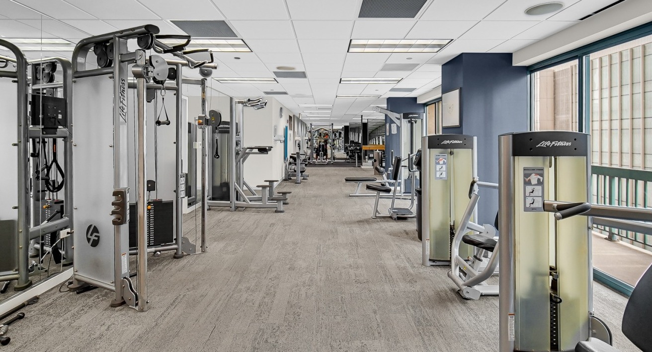Fitness center at One Superior Place Apartments with Life Fitness machines, free weights, and large windows with city views