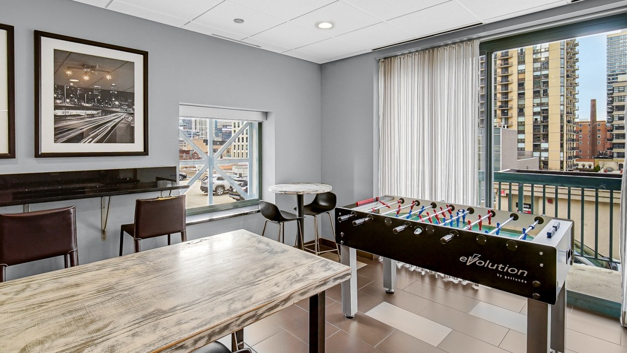 Game lounge at One Superior Place Apartments with foosball table, bar seating, and tall windows overlooking Chicago city views