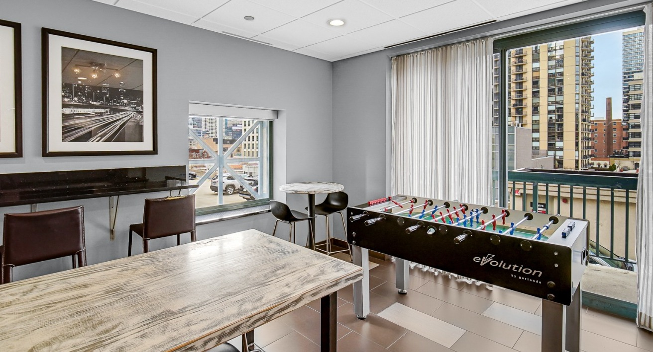 Game lounge at One Superior Place Apartments with foosball table, bar seating, and tall windows overlooking Chicago city views