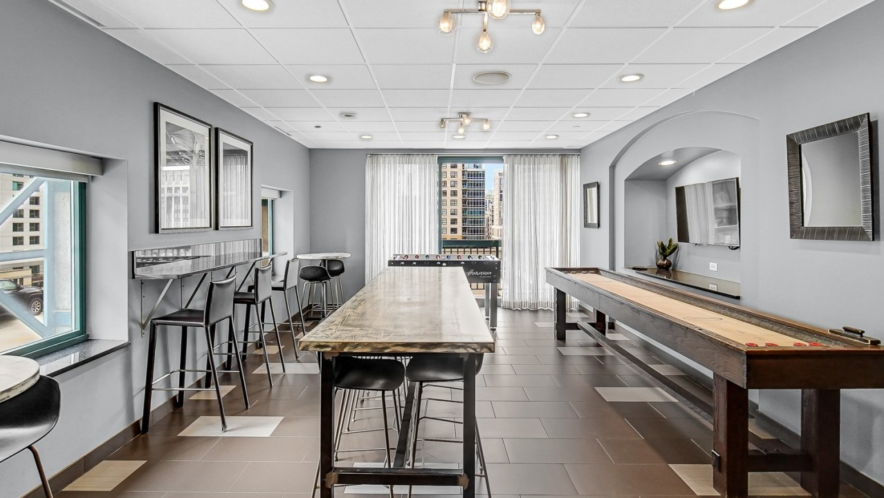 Resident game room at One Superior Place Apartments with shuffleboard table, high-top seating, and natural light from large windows
