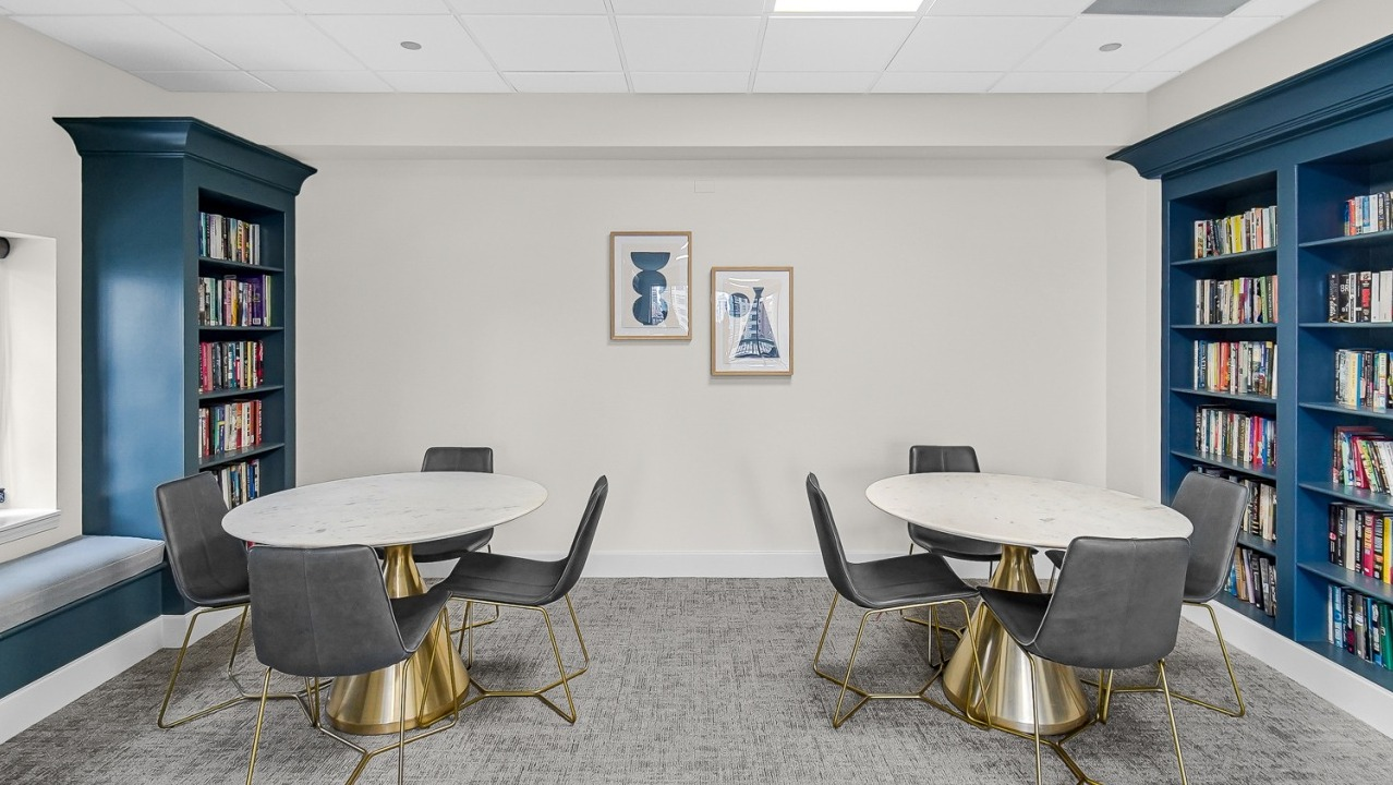 Comfortable library seating area with round tables, chairs, and bookshelves at One Superior Place apartments in Chicago