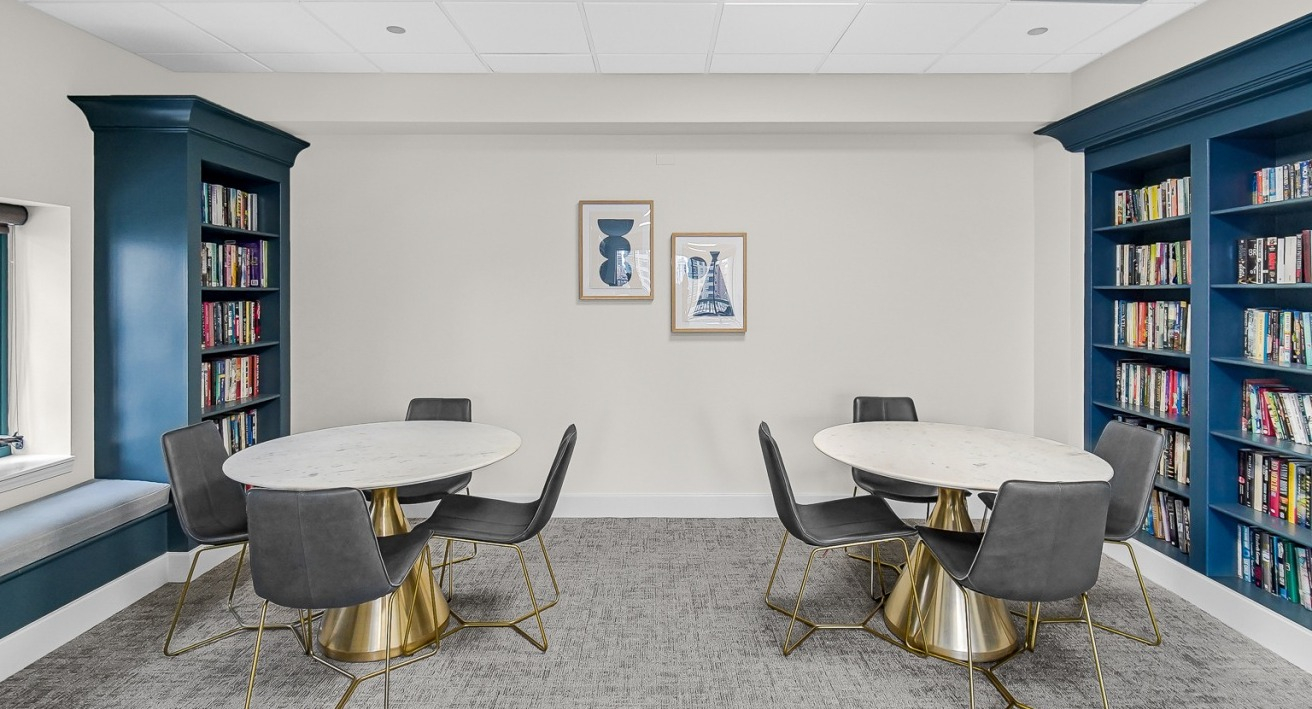 Comfortable library seating area with round tables, chairs, and bookshelves at One Superior Place apartments in Chicago