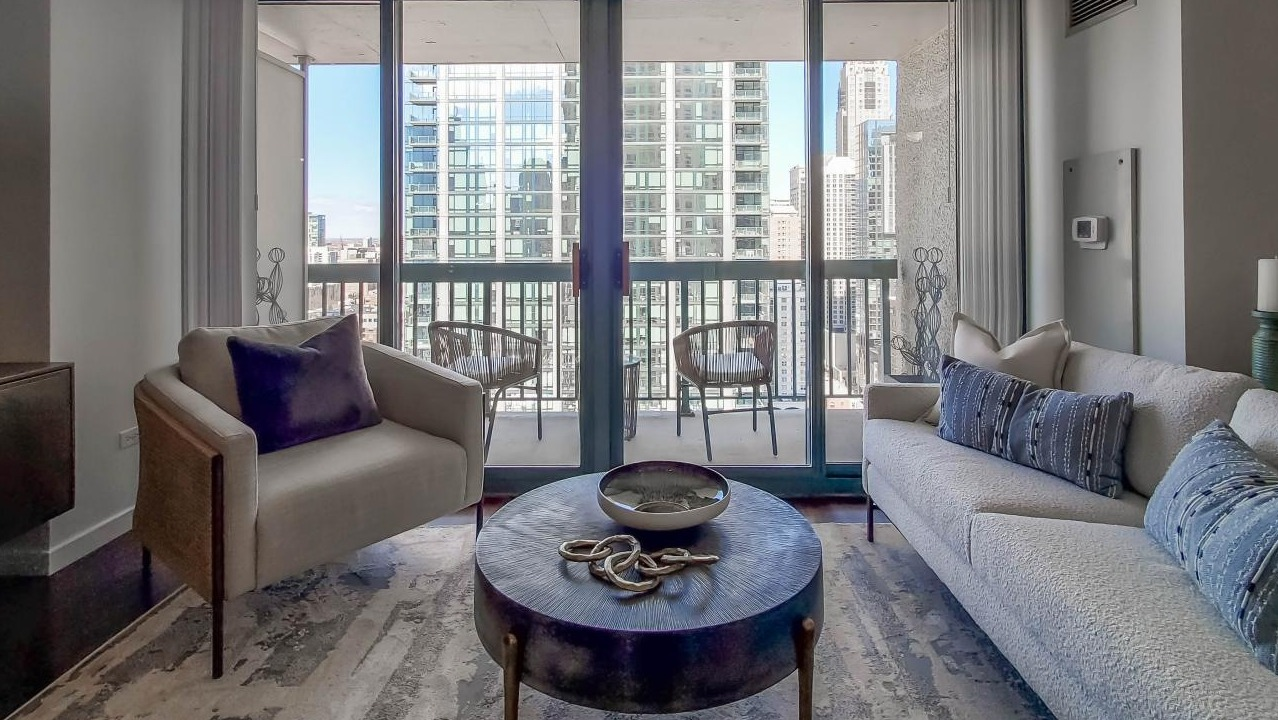Living room at One Superior Place Apartments with plush seating, glass coffee table, and direct balcony access overlooking downtown Chicago