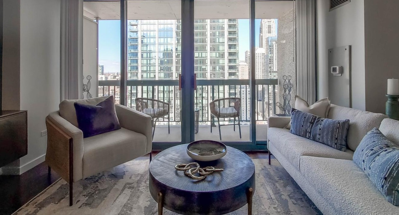 Living room at One Superior Place Apartments with plush seating, glass coffee table, and direct balcony access overlooking downtown Chicago