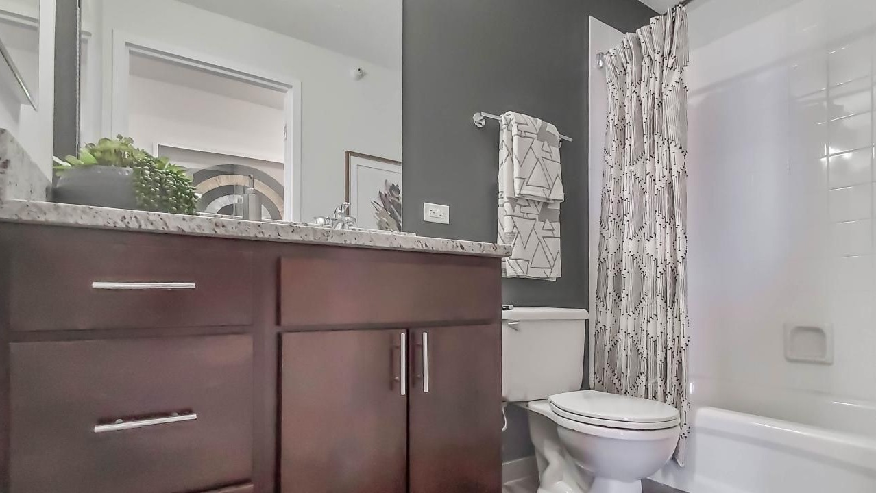 Modern bathroom at One Superior Place Apartments with granite countertop, dark wood vanity, and a white tub with patterned shower curtain