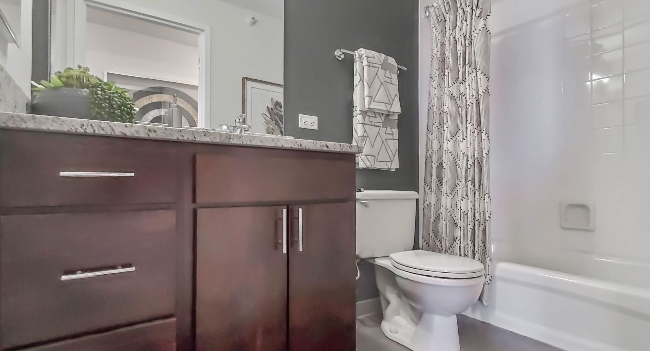 Modern bathroom at One Superior Place Apartments with granite countertop, dark wood vanity, and a white tub with patterned shower curtain