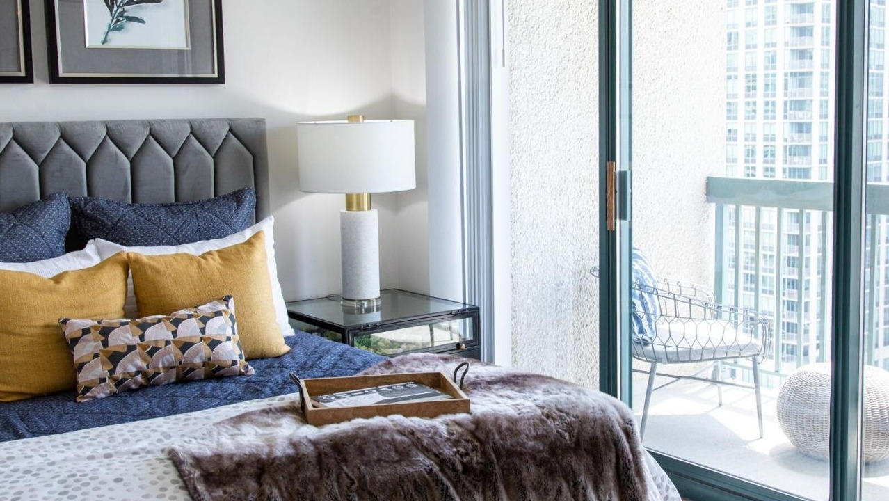 Bedroom at One Superior Place Apartments with upholstered headboard, cozy bedding, and sliding doors opening to a private balcony