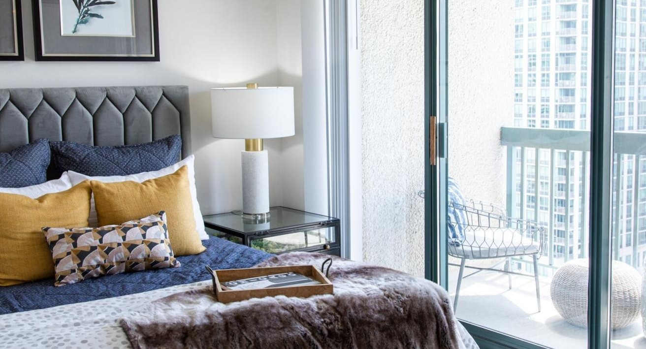 Bedroom at One Superior Place Apartments with upholstered headboard, cozy bedding, and sliding doors opening to a private balcony