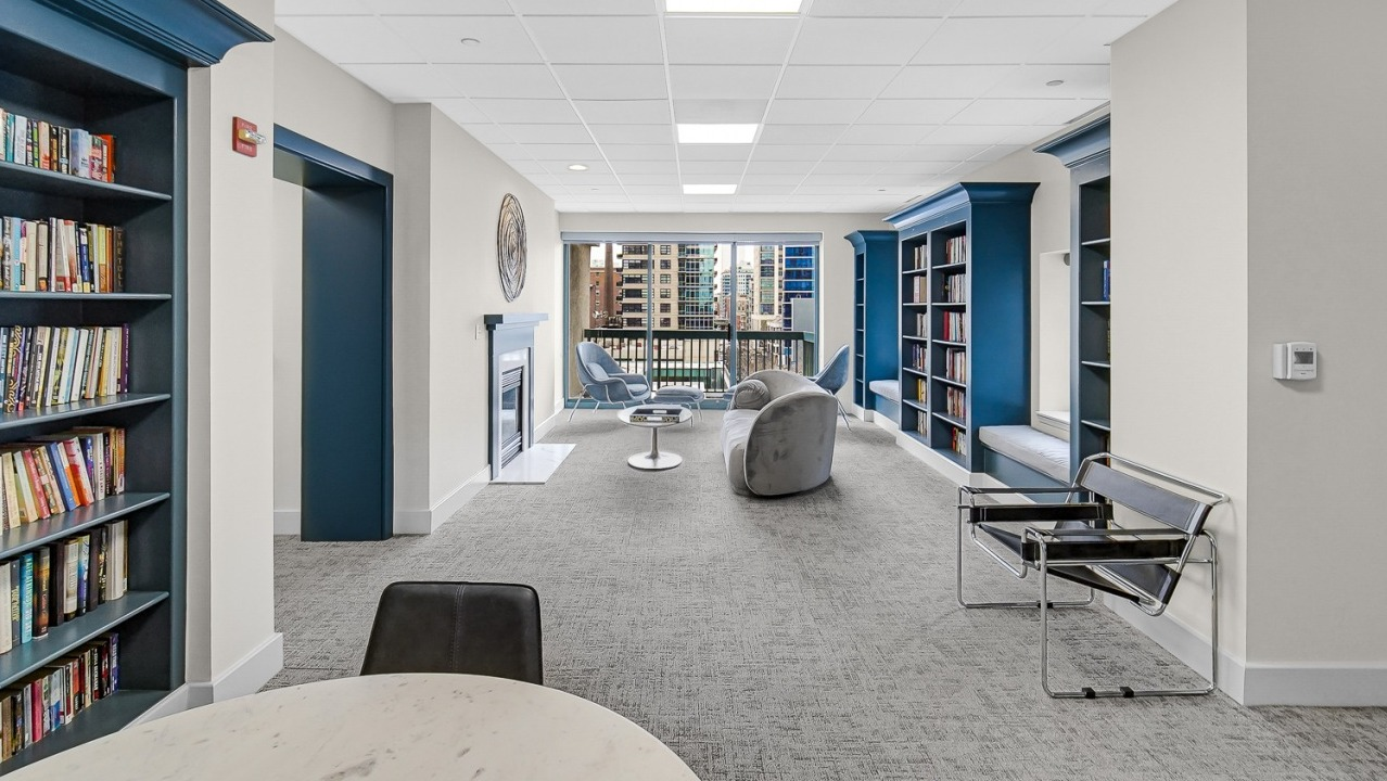 Bright library lounge with bookshelves, seating areas, and city views at One Superior Place apartments in Chicago