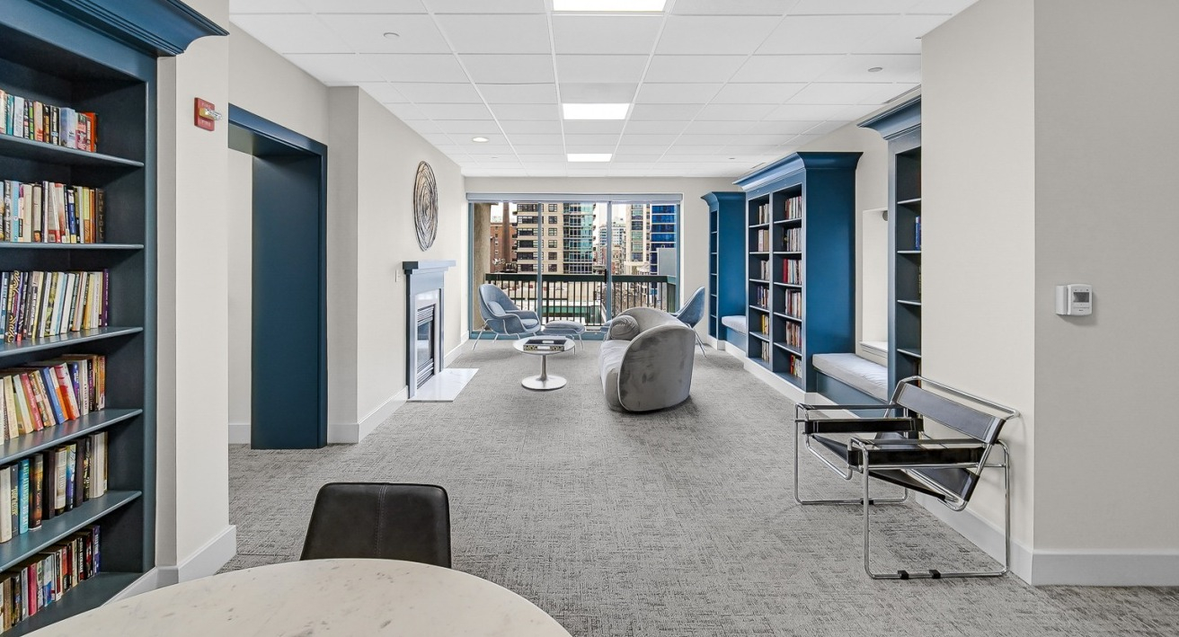 Bright library lounge with bookshelves, seating areas, and city views at One Superior Place apartments in Chicago