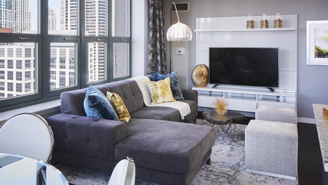 Stylish living room at One Superior Place Apartments with sectional couch, large TV, and expansive city views through tall windows