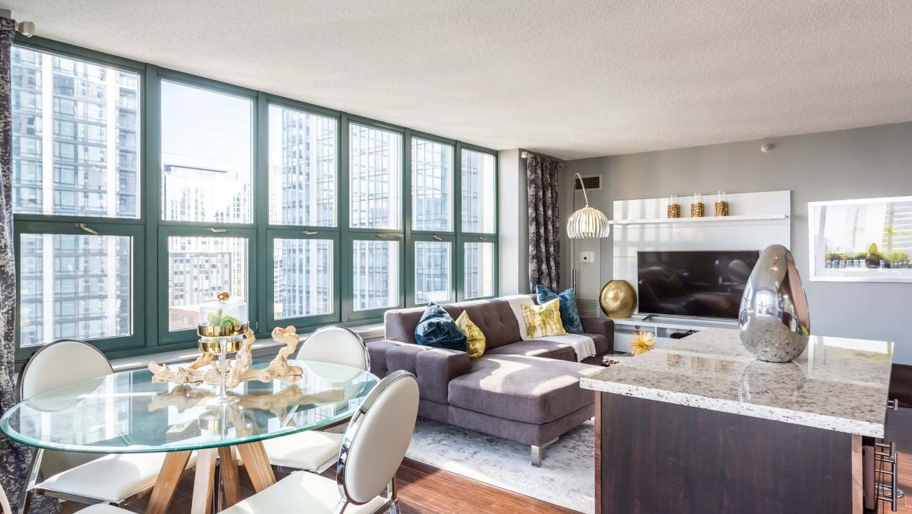 Spacious living and dining area at One Superior Place Apartments with sectional sofa, round glass dining table, and floor-to-ceiling windows