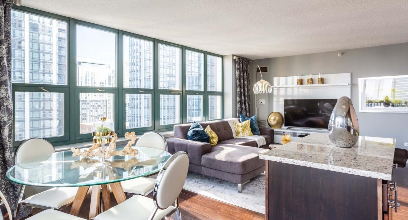 Spacious living and dining area at One Superior Place Apartments with sectional sofa, round glass dining table, and floor-to-ceiling windows