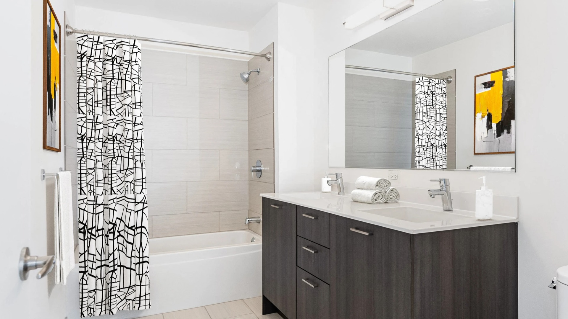Crisp bathroom with dark wood vanity, large mirror, tiled tub-shower, and bold black-and-white curtain at ONE333 apartments in Chicago, offering a clean modern look