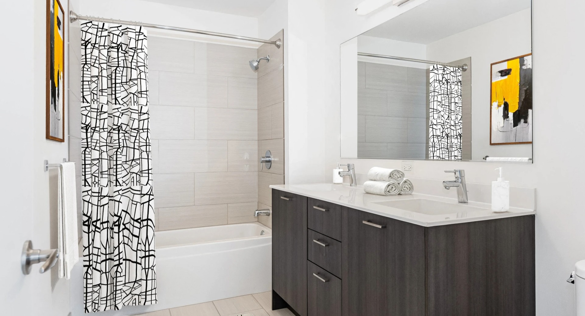 Crisp bathroom with dark wood vanity, large mirror, tiled tub-shower, and bold black-and-white curtain at ONE333 apartments in Chicago, offering a clean modern look
