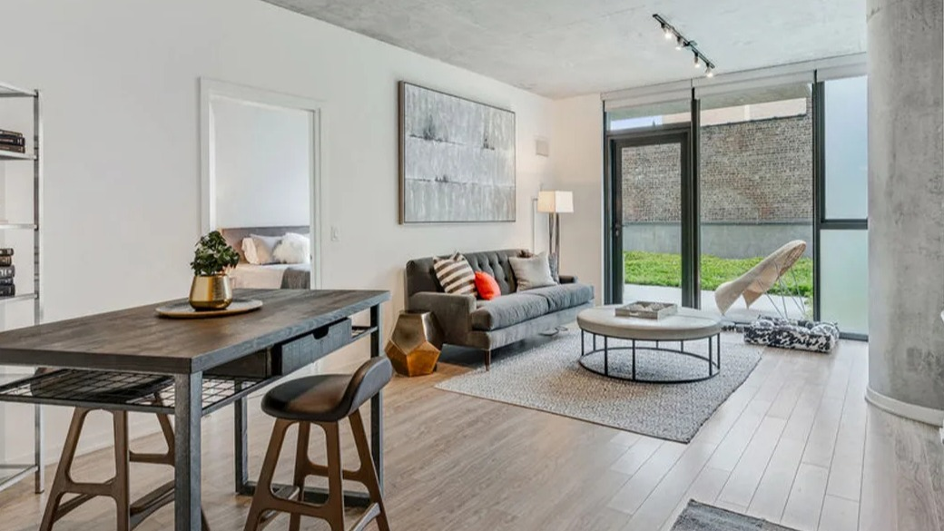 Bright living room at ONE333 apartments in Chicago with concrete ceiling, slider to patio and green space, plus flexible dining or home-office setu