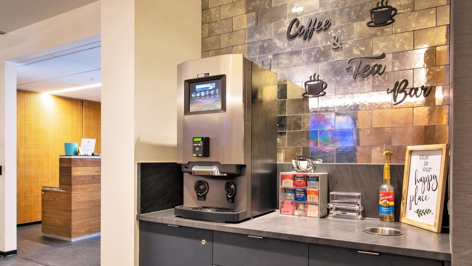 Resident coffee and tea bar at ONE333 apartments in Chicago with touchscreen brewer, condiments, and mirrored tile backsplash for quick morning pick-me-ups