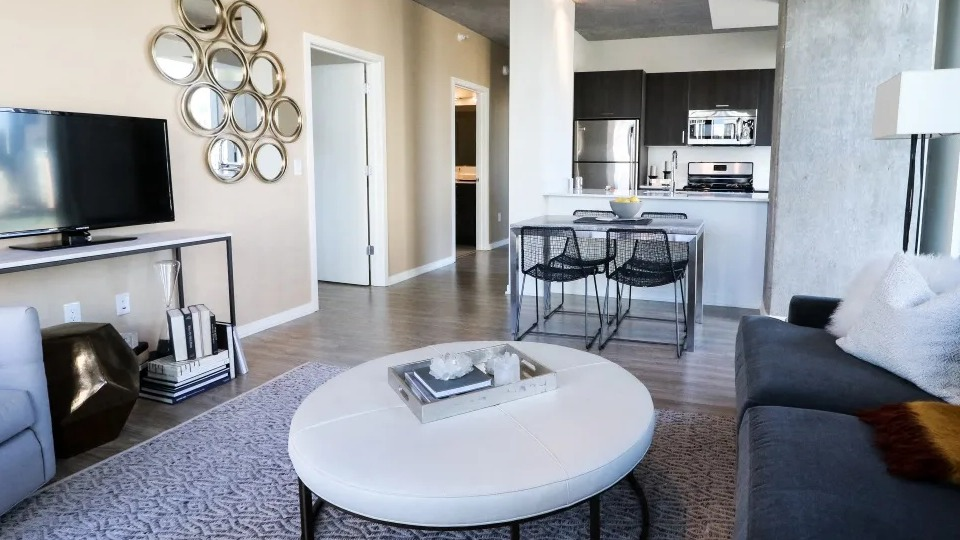Cozy open-concept living room with round coffee table, track lighting, and a modern kitchen island at ONE333 apartments in Chicago