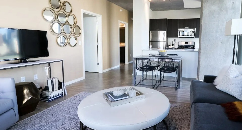 Cozy open-concept living room with round coffee table, track lighting, and a modern kitchen island at ONE333 apartments in Chicago