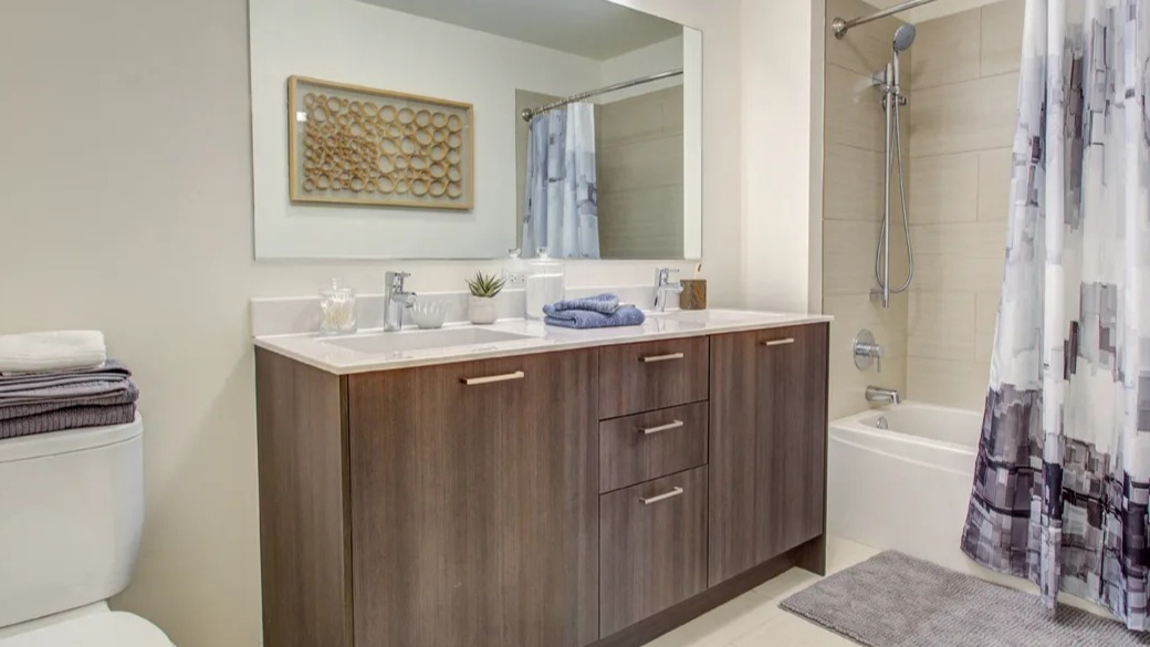 Modern bathroom with double vanity, wide mirror, and tiled tub-shower with handheld sprayer at ONE333 apartments in Chicago, designed for easy everyday living