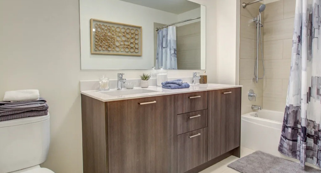 Modern bathroom with double vanity, wide mirror, and tiled tub-shower with handheld sprayer at ONE333 apartments in Chicago, designed for easy everyday living