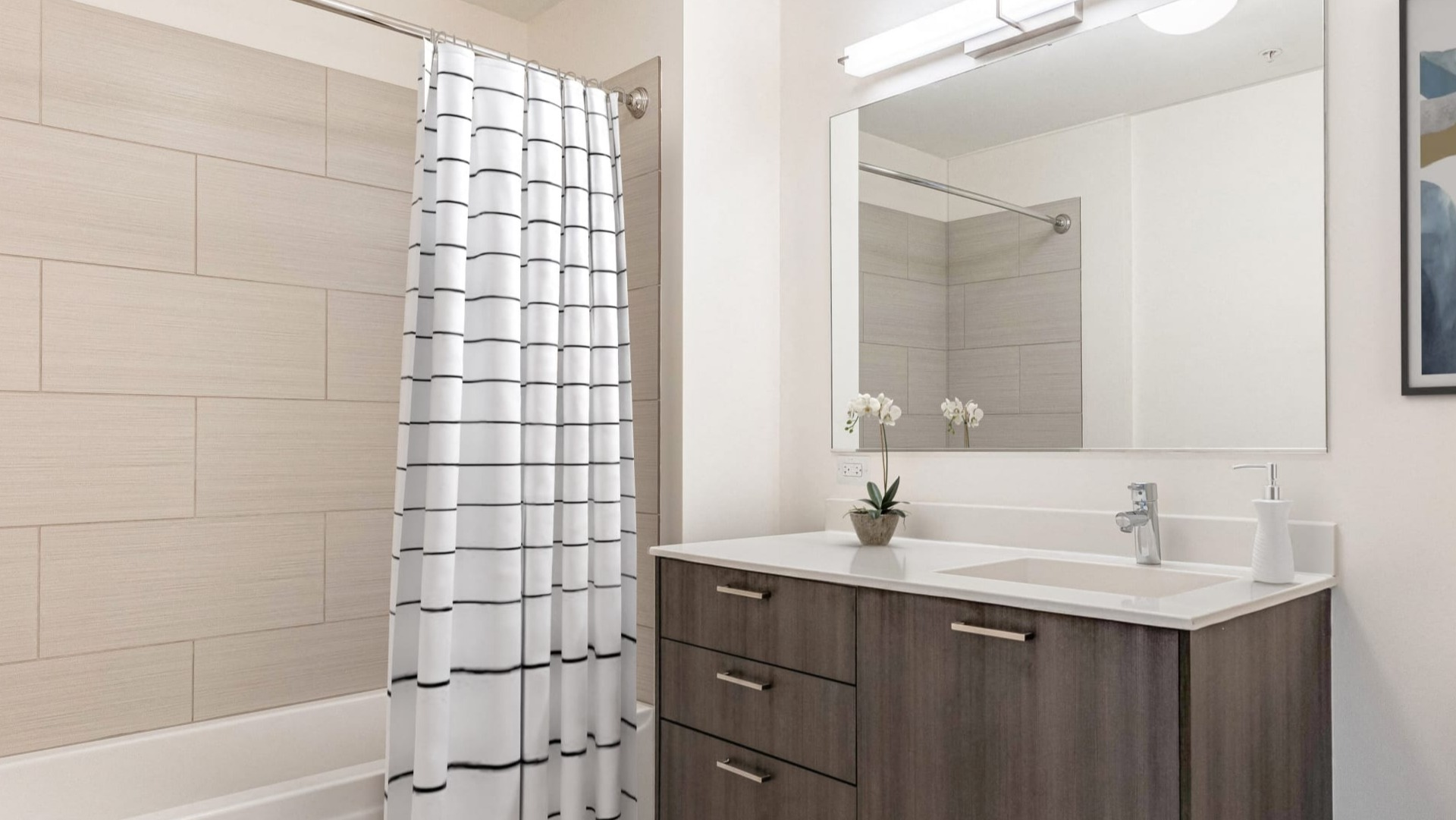 Modern bathroom with wide vanity, large mirror, and tiled tub-shower with striped curtain at ONE333 apartments in Chicago