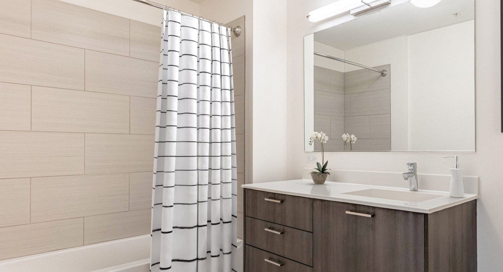 Modern bathroom with wide vanity, large mirror, and tiled tub-shower with striped curtain at ONE333 apartments in Chicago