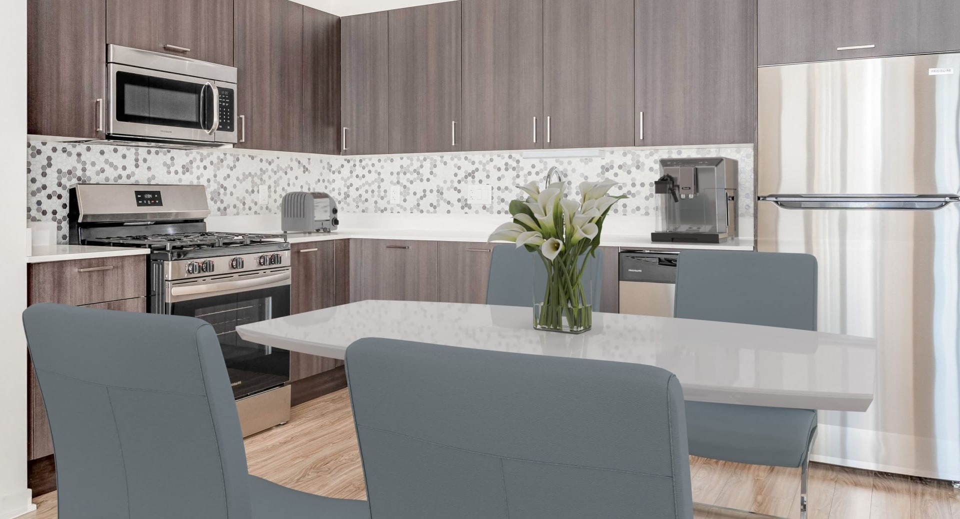 Contemporary kitchen with gray cabinets, hex tile backsplash, stainless appliances, and dining area at ONE333 apartments in Chicago
