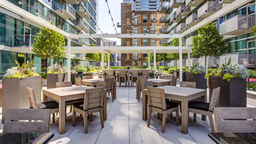 Spacious outdoor dining terrace with pergola, string lights, and modern tables at ONE333 apartments in Chicago—perfect for grilling and gatherings