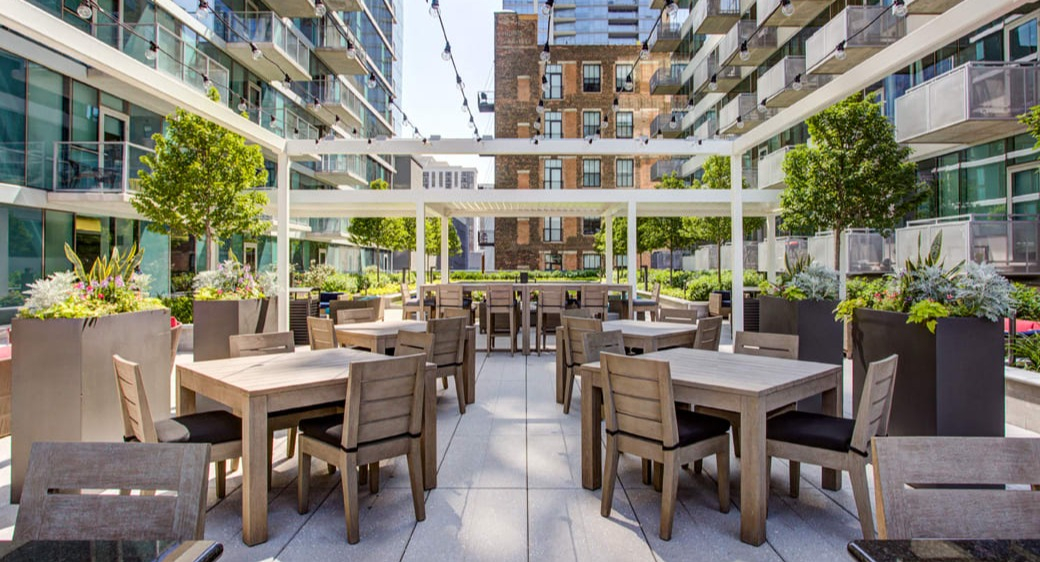 Spacious outdoor dining terrace with pergola, string lights, and modern tables at ONE333 apartments in Chicago—perfect for grilling and gatherings