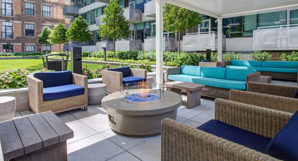 Outdoor lounge with fire pit, wicker seating, and landscaped courtyard at ONE333 apartments in Chicago, ideal for relaxing and hosting friends