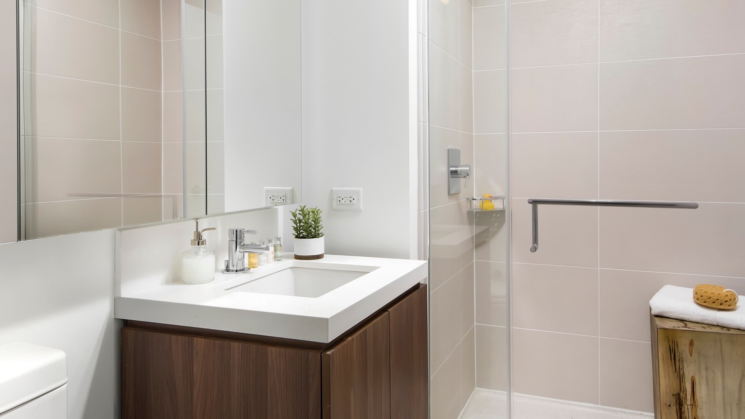 Modern apartment bathroom at OneEleven in Chicago, featuring a sleek vanity, mirror, and a spacious walk-in shower