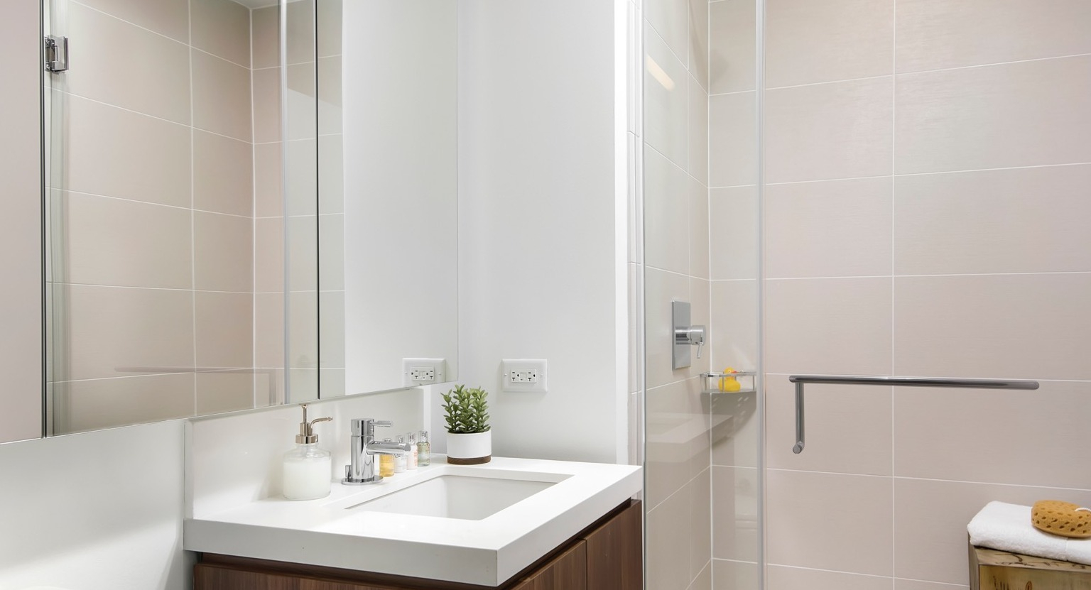 Modern apartment bathroom at OneEleven in Chicago, featuring a sleek vanity, mirror, and a spacious walk-in shower