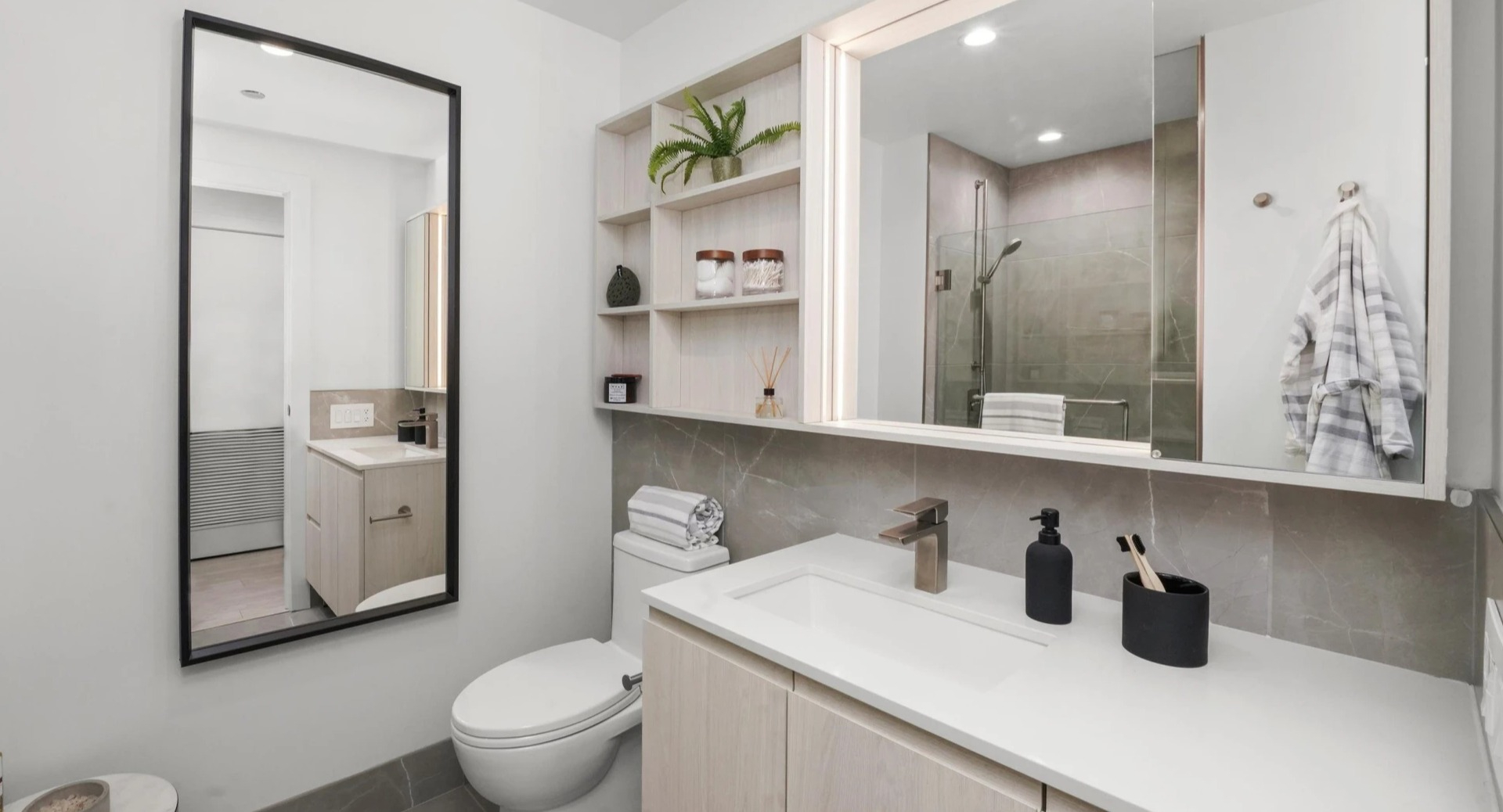 Modern apartment bathroom at Onni Fulton Market in Chicago, featuring a sleek vanity, mirror, and a contemporary toilet