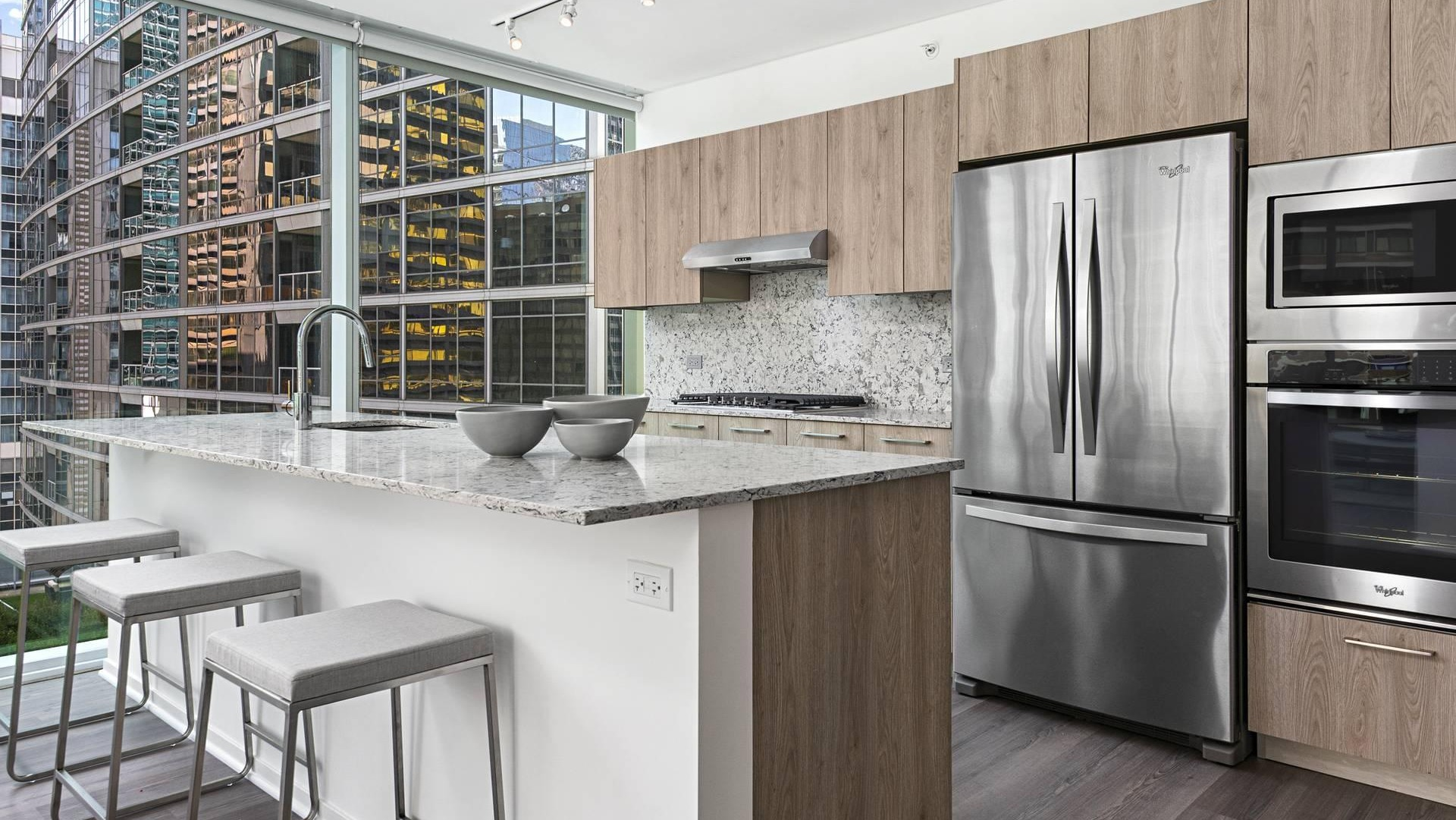 Chef-style kitchen at Optima Signature with island breakfast bar, stainless appliances, and stone counters framed by skyline views