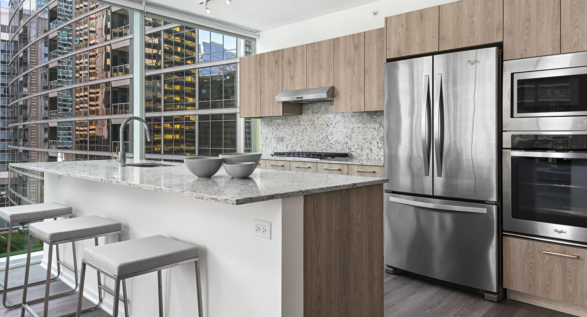 Chef-style kitchen at Optima Signature with island breakfast bar, stainless appliances, and stone counters framed by skyline views